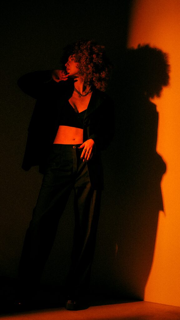 Confident woman in a structured outfit standing in soft red lighting, representing intentional presence and quiet influence