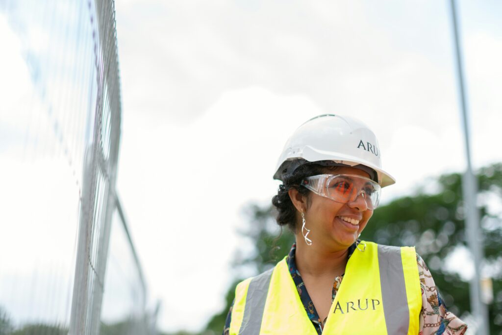 A smiling woman wearing an engineer's helmet and reflector